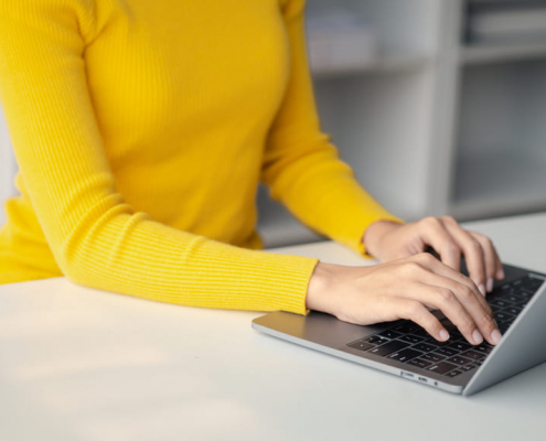 Frau in gelbem Pulli schreibt auf Laptop- Office Management Alexa - Virtuelle Assistenz - 04