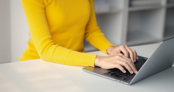Frau in gelbem Pulli schreibt auf Laptop- Office Management Alexa - Virtuelle Assistenz - 04